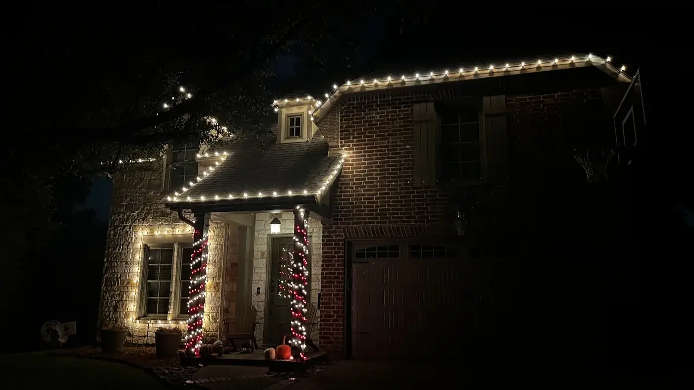 Warm white C9 roofline lights and red-and-white wrapped porch columns on a brick and stone DFW home
