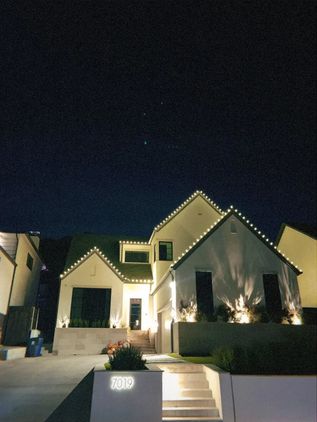 Warm white C9 Christmas lights tracing the gables of a modern white DFW home at night