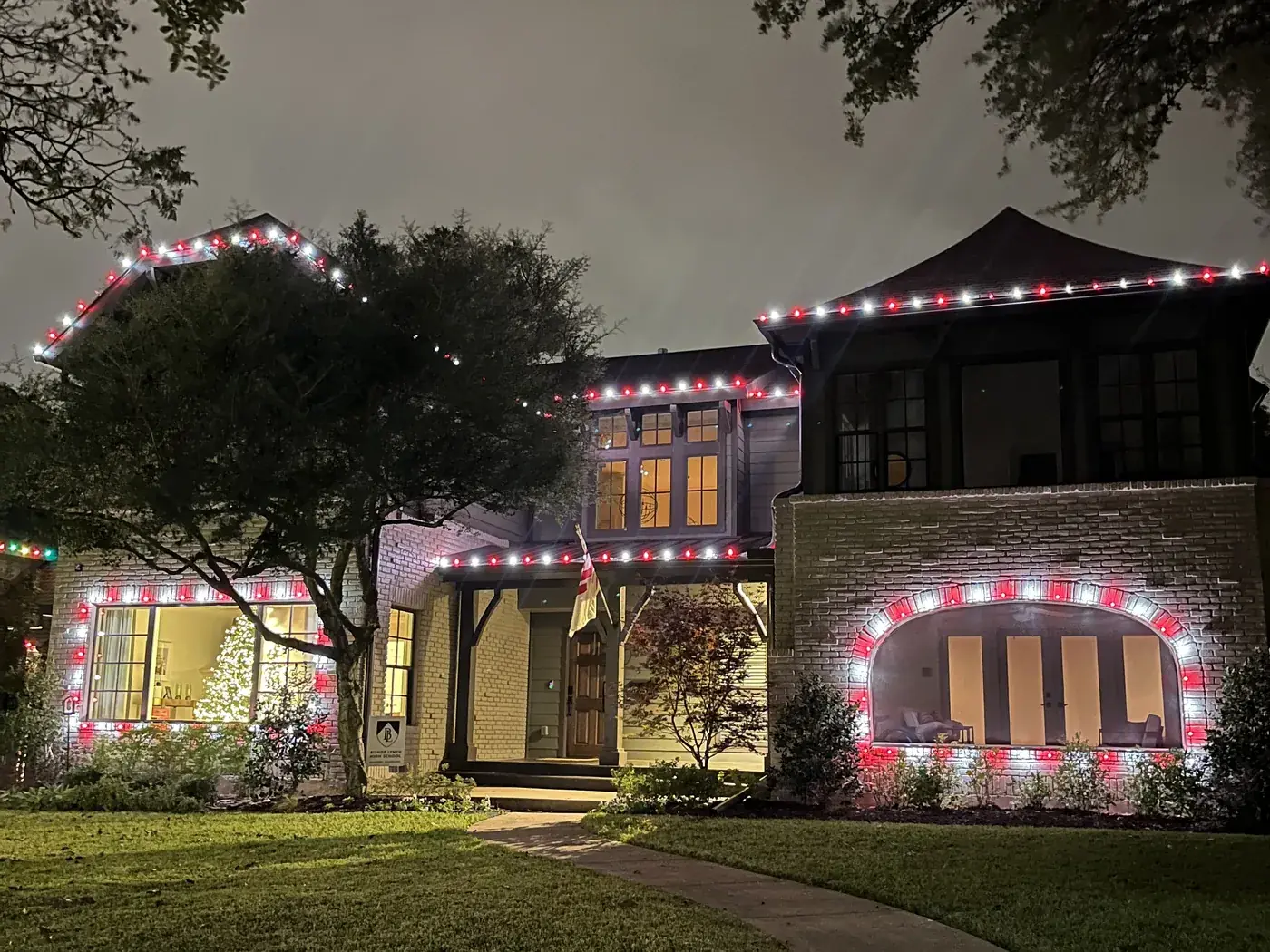 Red and white C9 Christmas lights outlining the roofline and arched windows of a two-story DFW home at night