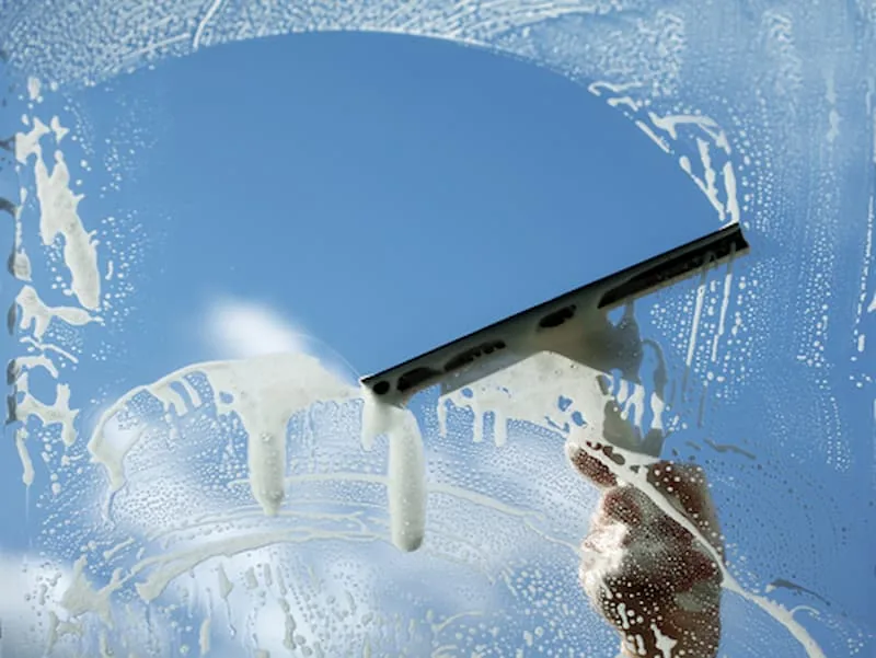 Professional squeegee pulling soap from a window pane, leaving streak-free glass